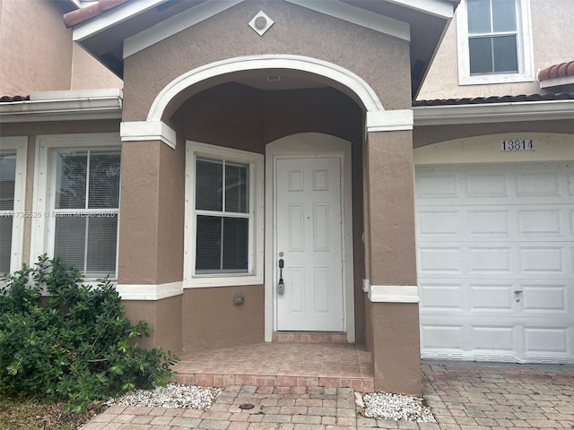 doorway to property featuring a garage, decorative driveway, and stucco siding