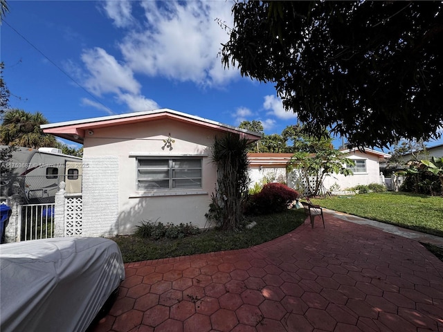 view of front facade featuring a patio area, stucco siding, a front yard, and fence