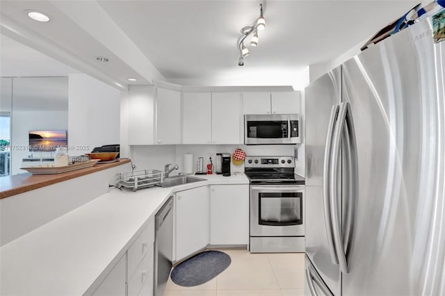 kitchen featuring light tile patterned floors, stainless steel appliances, a sink, and white cabinetry