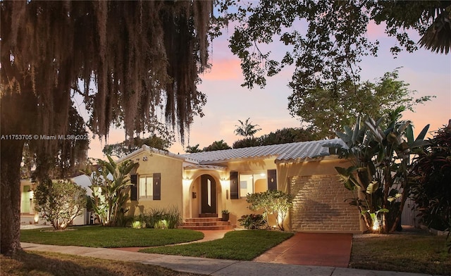 view of front of house with a yard, a tiled roof, and stucco siding