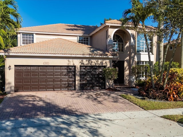 view of front facade with an attached garage, a tile roof, decorative driveway, and stucco siding