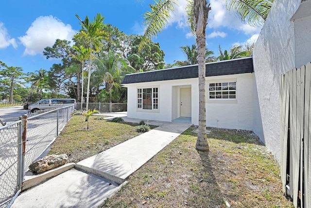 property entrance featuring roof with shingles, fence, and stucco siding