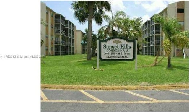 community sign featuring uncovered parking and a lawn