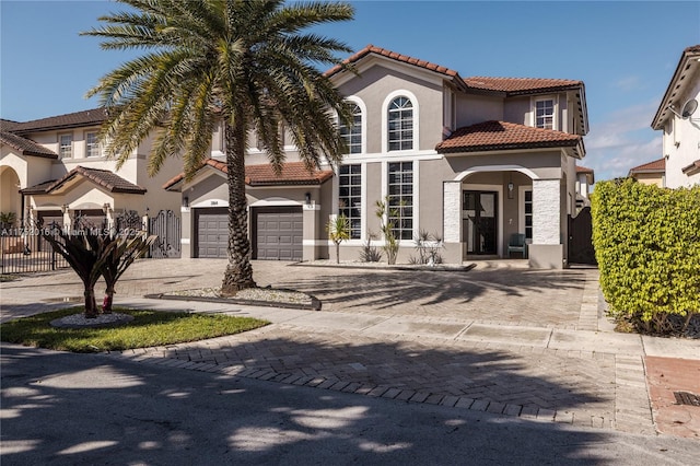 mediterranean / spanish home featuring driveway, a tile roof, an attached garage, fence, and stucco siding