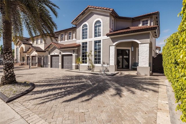 mediterranean / spanish-style home featuring driveway, an attached garage, a gate, and stucco siding