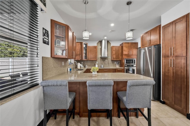 kitchen with a peninsula, stainless steel appliances, a sink, wall chimney exhaust hood, and tasteful backsplash