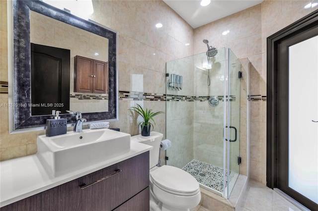 bathroom featuring tile walls, toilet, a shower stall, vanity, and tile patterned floors