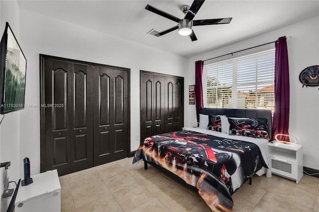 bedroom featuring light tile patterned floors, ceiling fan, baseboards, and two closets