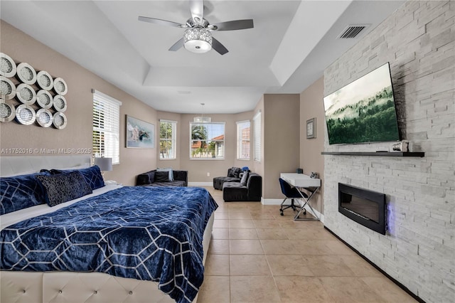 bedroom with baseboards, visible vents, a raised ceiling, a stone fireplace, and light tile patterned flooring