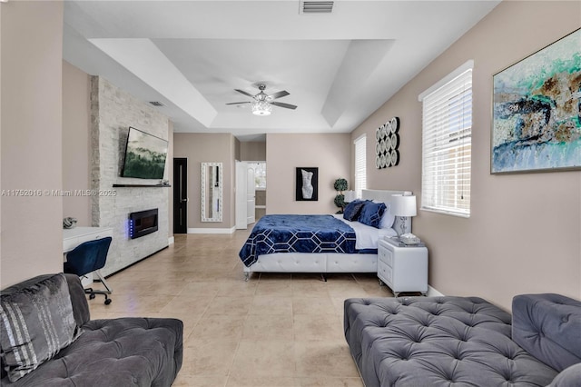 bedroom featuring a tray ceiling, light tile patterned floors, visible vents, a large fireplace, and baseboards