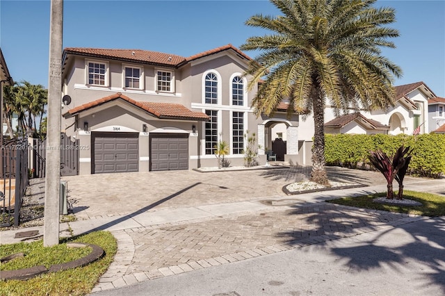 mediterranean / spanish-style house with an attached garage, fence, a tiled roof, decorative driveway, and stucco siding