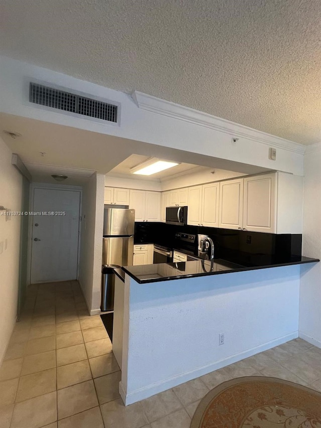 kitchen featuring dark countertops, visible vents, appliances with stainless steel finishes, a textured ceiling, and a peninsula