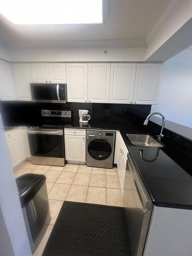 kitchen with light tile patterned floors, stainless steel appliances, a sink, white cabinetry, and washer / dryer