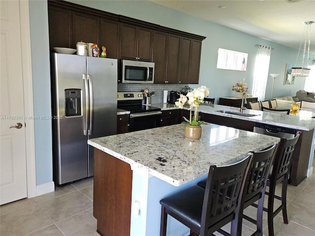 kitchen with dark brown cabinets, light tile patterned floors, a peninsula, stainless steel appliances, and a sink