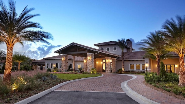 view of front of home with a tiled roof, stucco siding, a chimney, decorative driveway, and stone siding