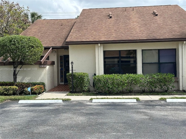 view of front of house with a shingled roof, uncovered parking, and stucco siding