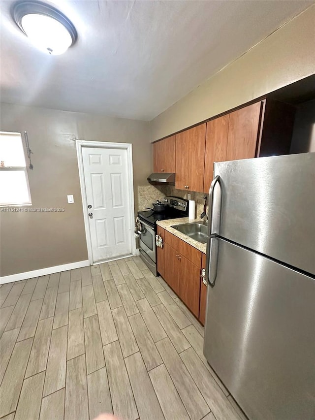 kitchen with brown cabinets, stainless steel appliances, wood finish floors, under cabinet range hood, and a sink