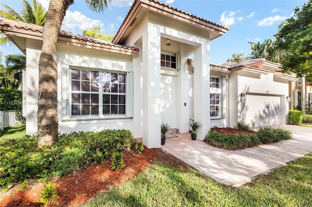 mediterranean / spanish-style house featuring decorative driveway, an attached garage, a tile roof, and stucco siding