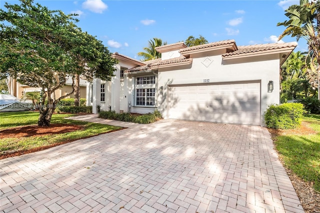 mediterranean / spanish house featuring a garage, a tiled roof, decorative driveway, and stucco siding