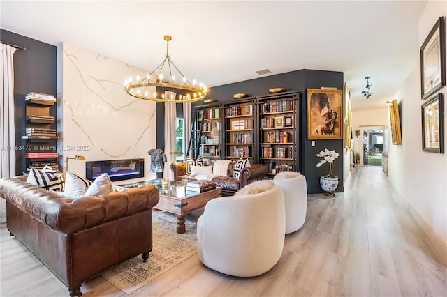 sitting room with light wood finished floors, baseboards, visible vents, an inviting chandelier, and a fireplace