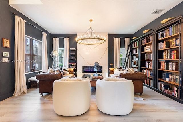 sitting room featuring visible vents, a notable chandelier, a premium fireplace, and wood finished floors