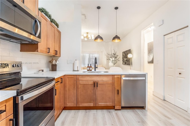 kitchen with a peninsula, a sink, light countertops, appliances with stainless steel finishes, and decorative backsplash