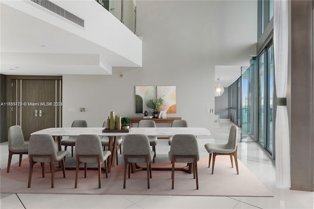 dining area with a notable chandelier, light tile patterned floors, visible vents, a towering ceiling, and a wall of windows