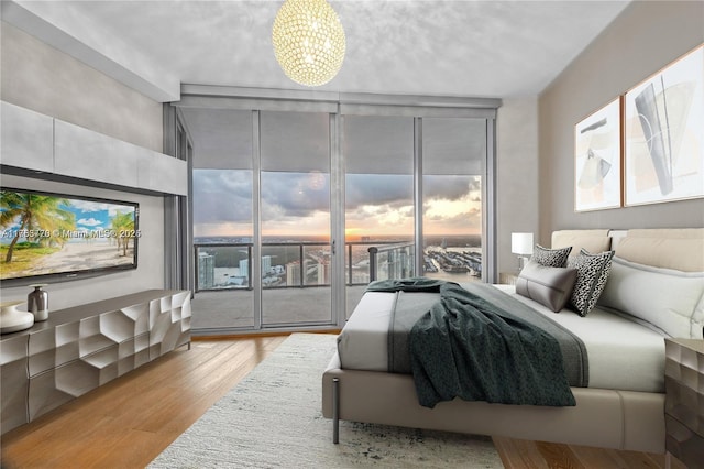 bedroom with a wall of windows, light wood-type flooring, a chandelier, and access to outside