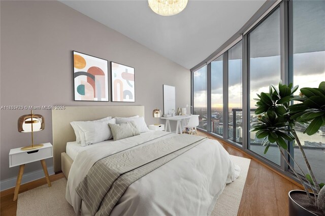 bedroom featuring lofted ceiling, expansive windows, baseboards, and wood finished floors