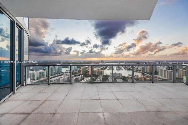 balcony at dusk featuring a water view and a city view