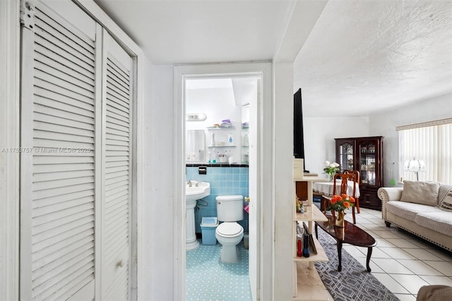 interior space with a textured ceiling, light tile patterned floors, wainscoting, and tile walls