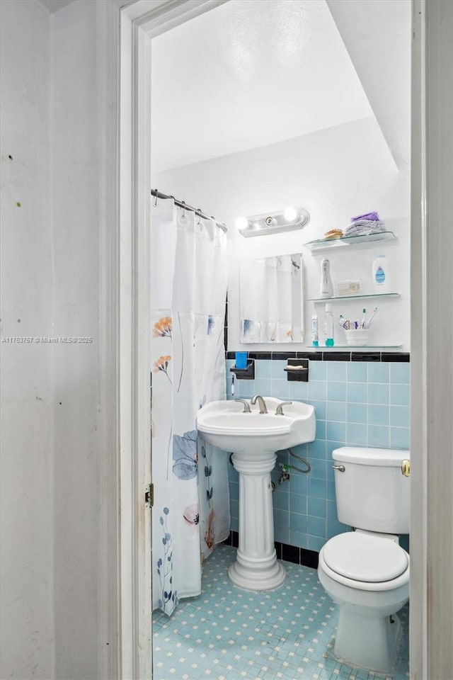 bathroom featuring tile walls, a shower with shower curtain, toilet, tile patterned floors, and a sink