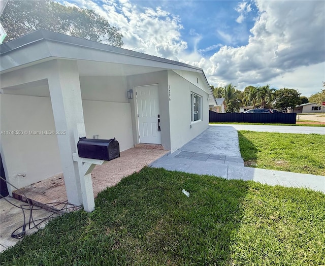 view of side of home with stucco siding, fence, and a yard