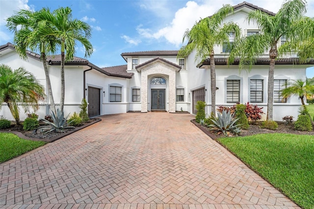 mediterranean / spanish house featuring an attached garage, a tile roof, decorative driveway, and stucco siding