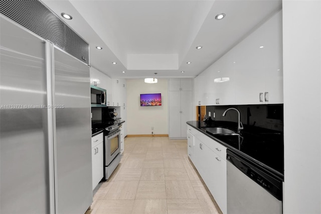 kitchen featuring dark countertops, stainless steel appliances, white cabinetry, a sink, and recessed lighting