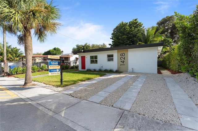 ranch-style home with a front yard, fence, and stucco siding