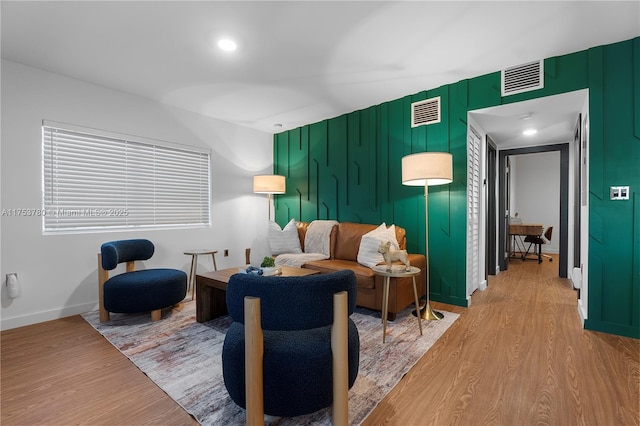 living room with light wood finished floors, visible vents, and an accent wall