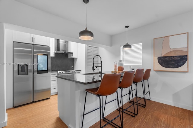 kitchen featuring a sink, light wood-style floors, stainless steel refrigerator with ice dispenser, a kitchen bar, and wall chimney exhaust hood