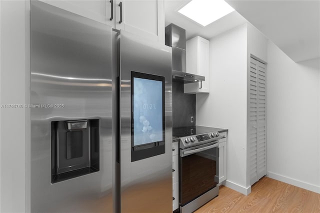 kitchen featuring baseboards, light wood finished floors, stainless steel appliances, white cabinetry, and wall chimney exhaust hood