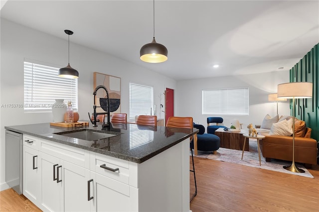 kitchen with light wood finished floors, open floor plan, pendant lighting, dishwashing machine, and a sink