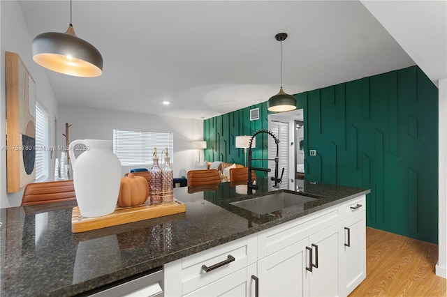 kitchen with dark stone counters, light wood-style flooring, a sink, hanging light fixtures, and white cabinetry