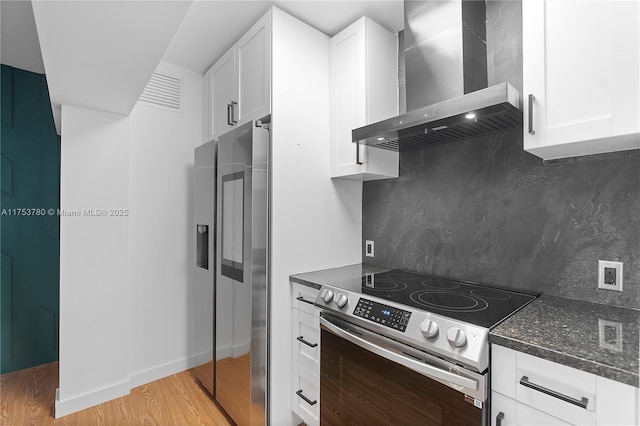 kitchen featuring white cabinetry, appliances with stainless steel finishes, wall chimney exhaust hood, light wood finished floors, and decorative backsplash