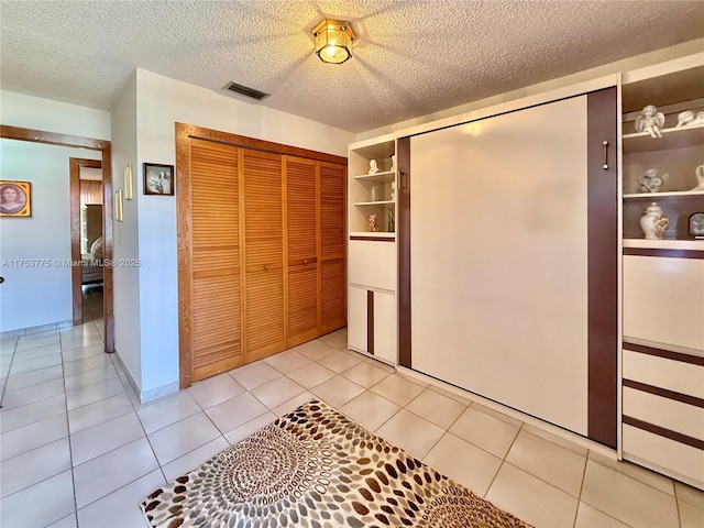 bedroom with a closet, visible vents, a textured ceiling, and light tile patterned floors