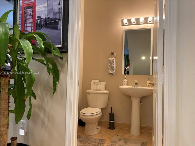 half bath with toilet, baseboards, and tile patterned floors