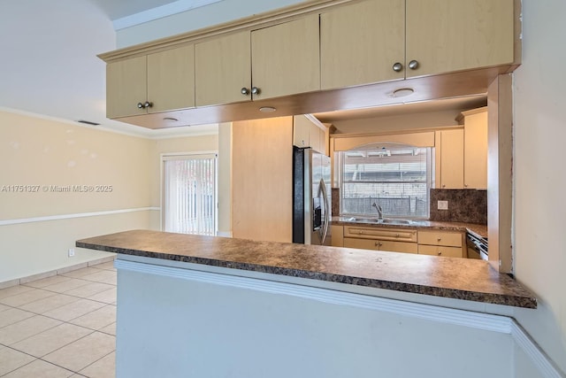 kitchen with backsplash, light tile patterned flooring, a sink, stainless steel fridge, and a peninsula