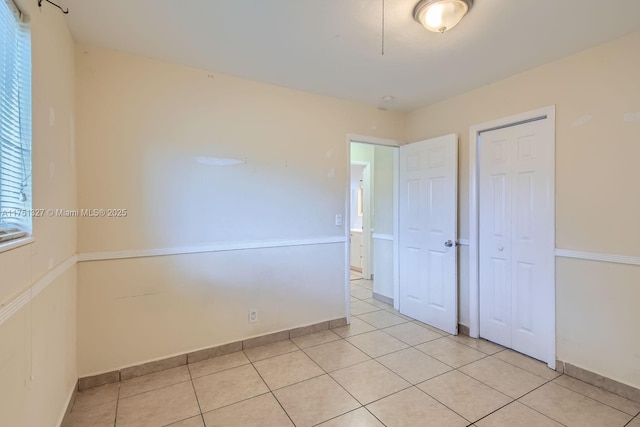 unfurnished bedroom with light tile patterned floors, a closet, and baseboards