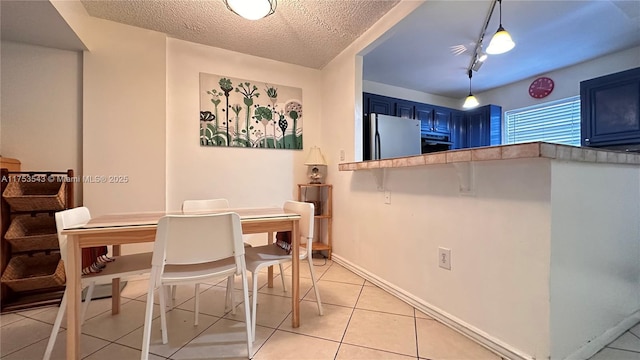 dining space featuring a textured ceiling, light tile patterned flooring, and baseboards