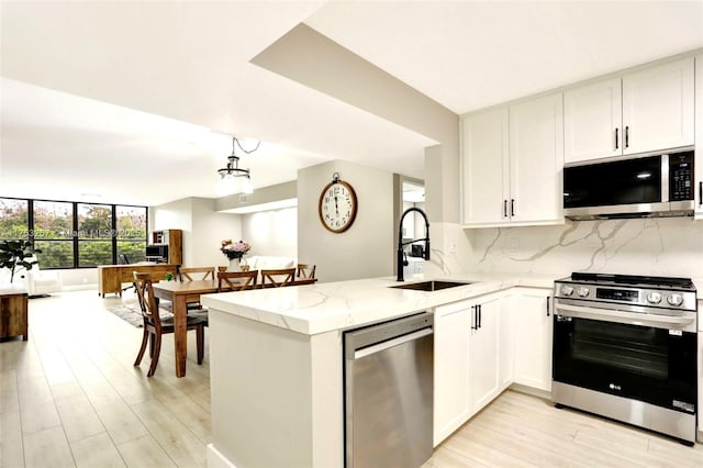 kitchen featuring decorative backsplash, appliances with stainless steel finishes, a sink, light stone countertops, and a peninsula