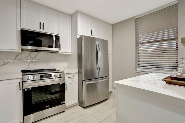 kitchen with light stone countertops, white cabinetry, stainless steel appliances, and backsplash