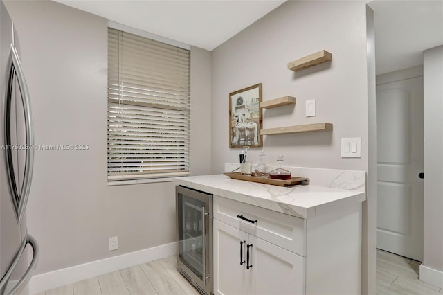 kitchen with beverage cooler, white cabinetry, baseboards, freestanding refrigerator, and light stone countertops